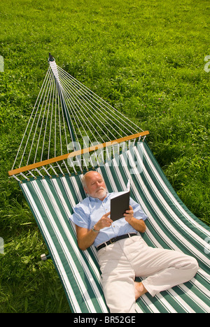 Älterer Herr liegen in der Hängematte, ein Buch zu lesen Stockfoto