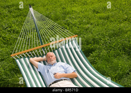 Älterer Herr liegen in der Hängematte und Musik hören Stockfoto