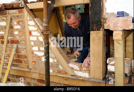 Renovierung einer alten Holz gerahmt Gebäude Maurer bilden eine neue Mauer mit alten Ziegeln und neue Eichenbalken auf einer Außenwand Stockfoto