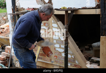 Renovierung einer alten Holz gerahmt Gebäude Maurer verwendet eine Kelle, eine alte Ziegel zu gestalten Stockfoto