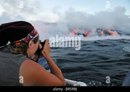 Frau auf Boot fotografieren Dampf steigt aus Lava fließt ins Meer, Kilauea-Vulkan, Hawaii Inseln, Vereinigte Staaten Stockfoto