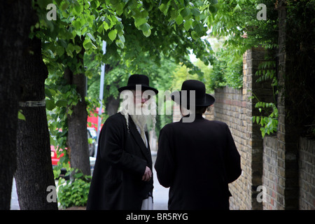 Zwei ältere orthodoxe jüdische Männer Bärte tragen schwarze Mäntel und Hüte, die im Chat auf dem Bürgersteig eines Baumes gesäumten Straße. Stockfoto