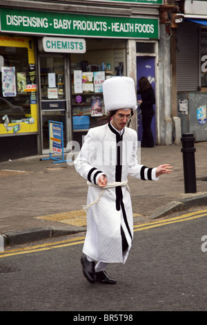 Ein kleiner Junge wie Purim Rabbiner in weiße Gewänder gekleidet und ein weißen hoher pelziger Hut kreuzt Dunsmure Straße während Purim-Festival. Stockfoto