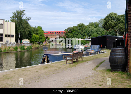 Die Wey Navigation am Dapdune Wharf in Guildford. Surrey. England. Mit Personenzug auf Eisenbahnbrücke. Stockfoto