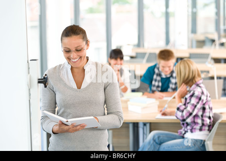 Lächelnde Lehrer mit Buch und Schüler an der High School im Klassenzimmer Stockfoto