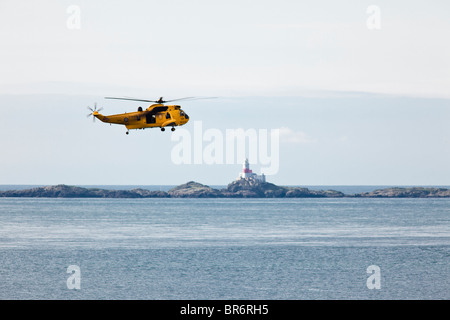 RAF-Rettungshubschrauber - Westland Sea King HAR3 über Church Bay, Anglesey.  Die Schären Leuchtturm im Hintergrund. Stockfoto