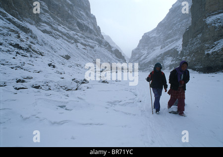 Zwei Schulmädchen auf zugefrorenen Fluss in fallenden Schnee zu Fuß. Stockfoto