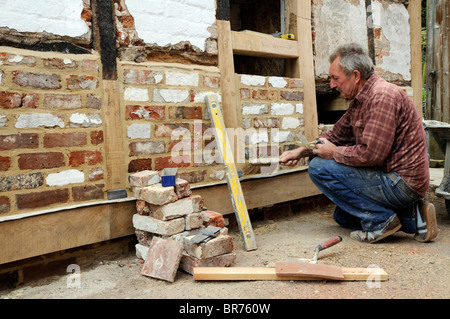 Renovierung einer alten Holz gerahmt Gebäude Maurer bilden eine neue Mauer mit alten Ziegeln und neue Eichenbalken auf einer Außenwand Stockfoto