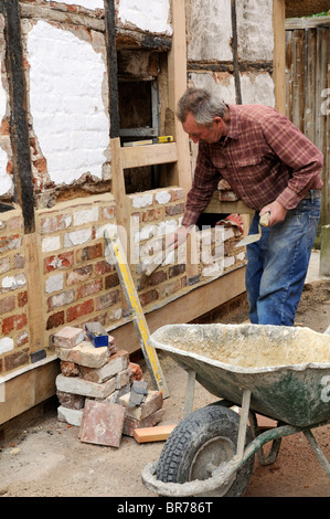 Renovierung einer alten Holz gerahmt Gebäude Maurer bilden eine neue Mauer mit alten Ziegeln und neue Eichenbalken auf einer Außenwand Stockfoto