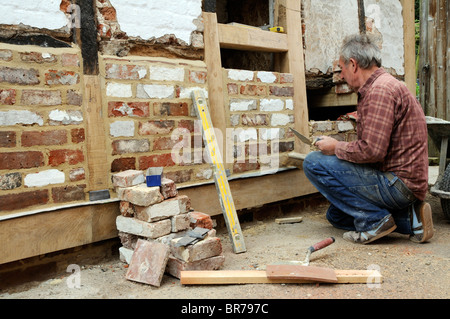 Renovierung einer alten Holz gerahmt Gebäude Maurer bilden eine neue Mauer mit alten Ziegeln und neue Eichenbalken auf einer Außenwand Stockfoto