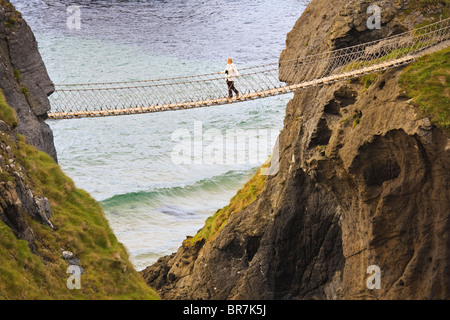 Junge Frau, die Überquerung der Seilbrücke Carrick-a-Rede in der Nähe der Ortschaft Ballintoy auf der Küste von County Antrim, Nordirland Stockfoto