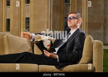 Wohlhabende junge Mann im Anzug auf einer Couch trinken und lesen Schundliteratur auf einer Art-Deco-Villa RC Harris Wasseraufbereitungsanlage Toronto Stockfoto