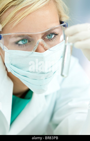 Eine blonde medizinische oder wissenschaftliche Forscher oder Arzt tragen Masken und Schutzbrillen, Blick auf eine klare Lösung in einem Labor Stockfoto