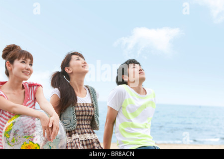 Drei junge Leute sitzen am Strand, Frau mit beach ball Stockfoto