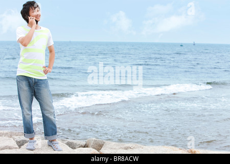 Junger Mann mit Handy am Strand Stockfoto