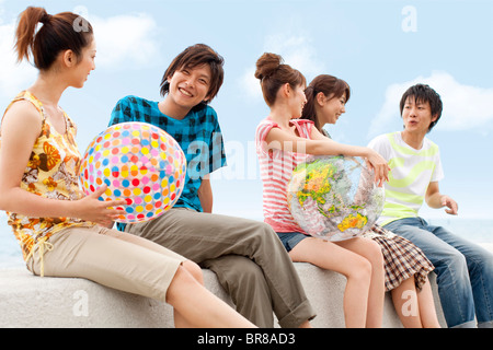 Fünf junge Leute sitzen auf Wellenbrecher, Frauen Strand Bälle Stockfoto