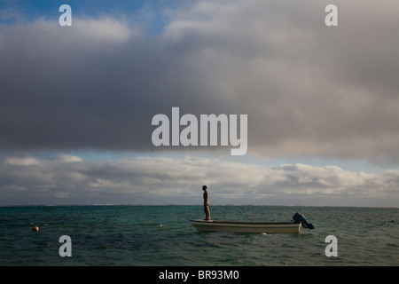 Ein junger Mann steht auf dem Bogen von seinem Fischerboot bereit, erfrischen Sie sich mit einem Sprung in den Ozean wie die Wolken über den Süden Stockfoto