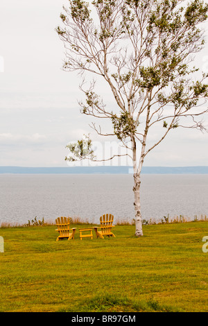 Zwei gelbe Adirondack Stühle und einen kleinen Tisch mit Blick aufs Wasser. Stockfoto