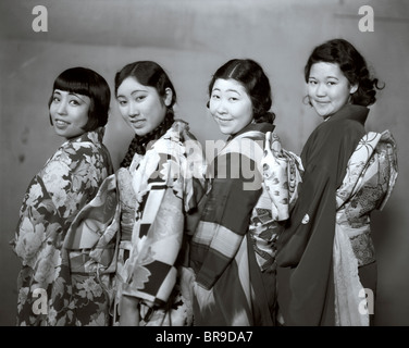 1920ER JAHREN VIER JUNGE JAPANERINNEN TRAGEN KIMONO LÄCHELNDEN BLICK IN DIE KAMERA Stockfoto