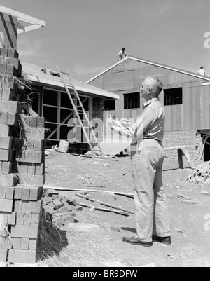 1950ER JAHRE ÄLTEREN MANN MIT ZWISCHENABLAGE AUF BAUSTELLE Stockfoto