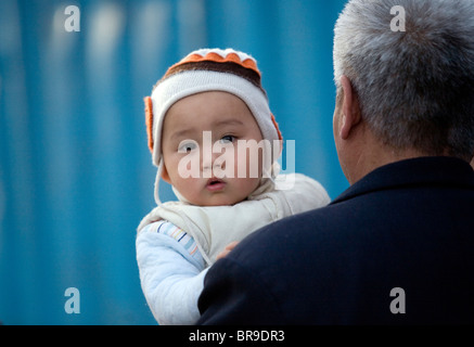 Ein Säugling blickt von seinem Großvater Schulter über wie sie zusammen ein Peking Straße China Fuß. Stockfoto