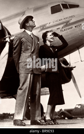 1930ER JAHREN GEHOBENE PAAR STEHEND AUF ASPHALT NEBEN FLUGZEUG Stockfoto