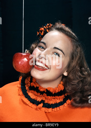 1940S 1950S LÄCHELNDE JUNGE FRAU TRAGEN HALLOWEENKOSTÜM-SCHAUKELN FÜR APPLE AN EINER SCHNUR Stockfoto