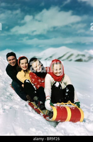 1940ER JAHRE GRUPPE VON DREI FRAUEN EIN MANN MIT ROTEN UND GELBEN RODEL RODELN IM WINTER SCHNEE Stockfoto