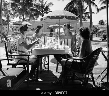 1930ER JAHREN DREI FRAUEN UND EIN MANN SITZT AM TROPISCHEN POOL BEISTELLTISCH MITEINANDER REDEN Stockfoto