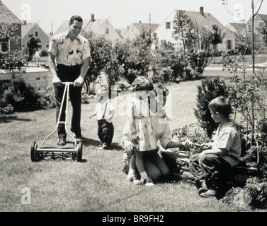 1950ER JAHRE FAMILIE IN HINTERHOF PAPA UND KLEINKIND SCHNEIDEN GRASS, MUTTER UND KINDER IM GARTEN Stockfoto