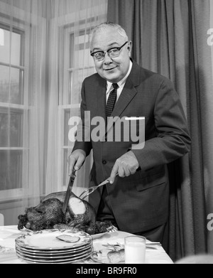 1960ER JAHRE MANN SCHNITZEN THANKSGIVING BRATEN TÜRKEI ABENDESSEN BLICK IN DIE KAMERA Stockfoto