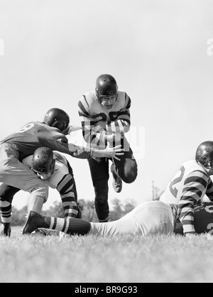 1950ER JAHREN FÜNF MÄNNER FUßBALL EIN SPIELER LAUFEN HOLDING BALL SPIELEN Stockfoto