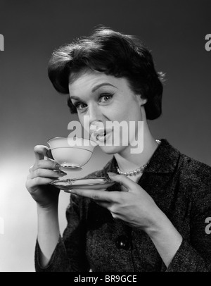 1950er Jahren 1960sWOMAN HOLDING Tasse und Untertasse trinken Tee oder Kaffee mit Blick in die Kamera Stockfoto