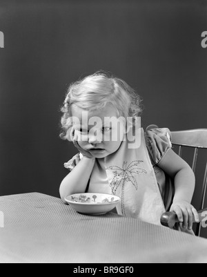 1930S 1940S TRAURIGE MÄDCHEN AM TISCH MIT MÜSLISCHALE Stockfoto