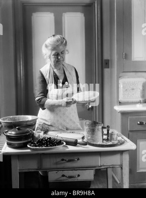 1920S 1930S SCHÜRZE FRAU GROßMUTTER TRAGEN CRIMP KRUSTE, SO DASS EIN KIRSCHKUCHEN Stockfoto