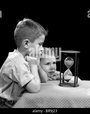 1940ER JAHREN ZWEI JUNGEN BEOBACHTEN SAND IN DER SANDUHR FALLEN WARTEN Stockfoto