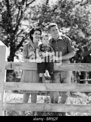 1940ER JAHREN LÄCHELN FRÖHLICHER FAMILIE MUTTER VATER KIND JUNGE PORTRAIT VON BAUERNHOF ZAUN Stockfoto