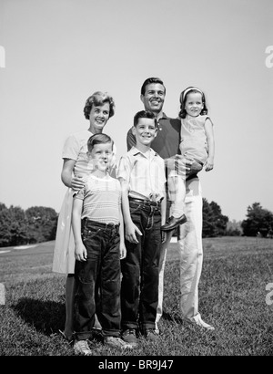 1960ER JAHREN LÄCHELND FAMILIENBILD AUF GRASS VATER MUTTER DREI KINDER STEHEN Stockfoto
