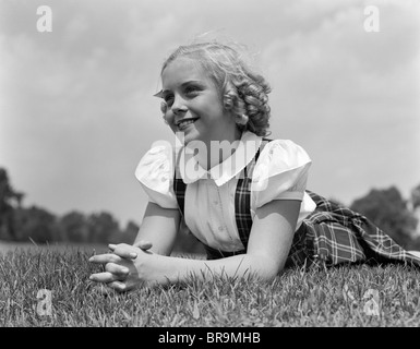 1940ER JAHRE BLONDE MÄDCHEN LÄCHELN AUF DEN LIPPEN LIEGEN AUF GRASS Stockfoto