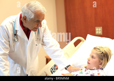 Älterer Arzt beugt sich Patienten in Pädiatrie Gemeinde Stockfoto