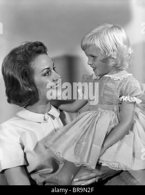 1960ER JAHRE WENIG BLONDE MÄDCHEN TRAGEN KOSTÜM SITZEN MIT MUTTER Stockfoto