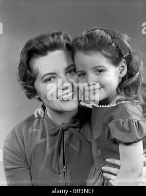 1950ER JAHRE MÄDCHEN TOCHTER LÄCHELND UMARMT FRAU MUTTER CHEEK TO CHEEK ZUSAMMEN Stockfoto