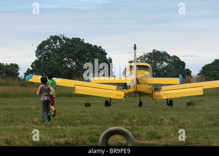 Zwei Kinder ein Fuji FA200 Aero Subaru einmotorigen Kunstflug Flugzeug herumlaufen, als ob es kriechen Stockfoto