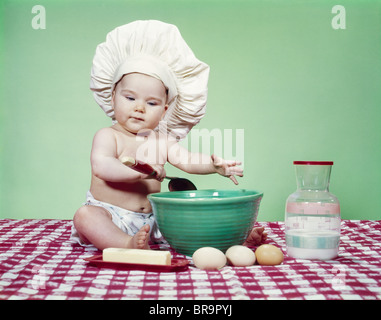 1960ER JAHREN TRAGEN KOCH HUT KINDERLÖFFEL SCHÜSSEL UND BACKEN ZUTATEN MISCHEN Stockfoto