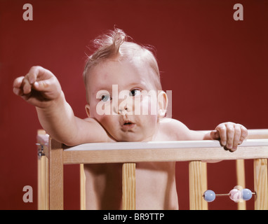 1960ER JAHRE BABY REACHING OUT VON KRIPPE Stockfoto