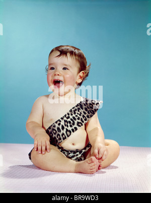 1960ER JAHREN LACHEN GLÜCKLICHES BABY MUND WEIT OFFEN TRAGEN LEOPARD PRINT TARZAN HÖHLENMENSCH KOSTÜM Stockfoto