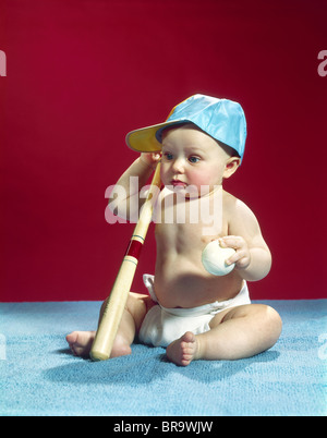 1960ER JAHRE BABY TRAGEN BLAUE BASEBALL-CAP MIT BALL UND SCHLÄGER Stockfoto