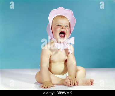 1960ER JAHREN ÜBERPRÜFT BABY TRAGEN ROSA HAUBE LACHEN Stockfoto