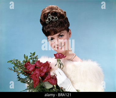 1960ER JAHREN TEENAGER SCHÖNHEIT KÖNIGIN HOLDING ROTE ROSEN TRAGEN PELZSTOLA UND TIARA BLICK IN DIE KAMERA Stockfoto