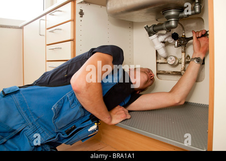 Heizungs- und Sanitär-Techniker reparieren die undichten Rohren unter der Küchenspüle Stockfoto